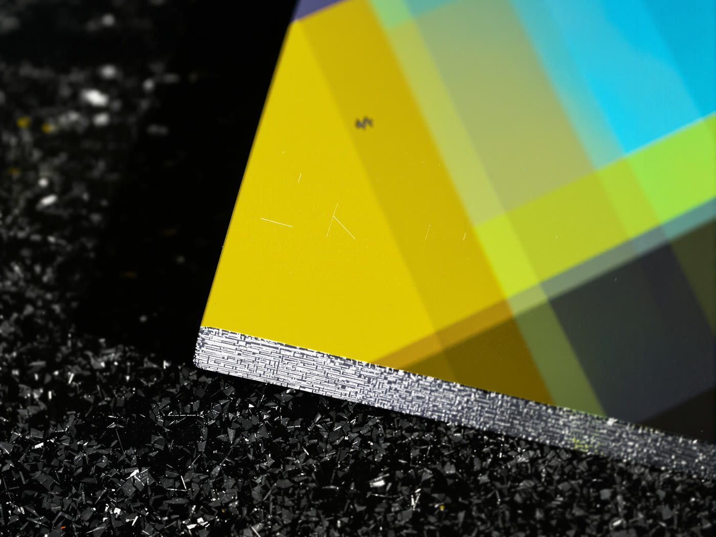 Macro detail of full-color UV ink sitting proud on brushed aluminum, the grain visible through the ink.